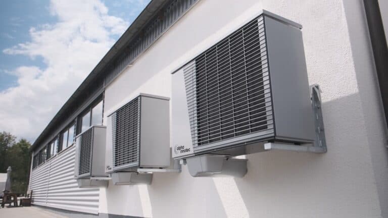Three gray air conditioning units mounted on a white wall.